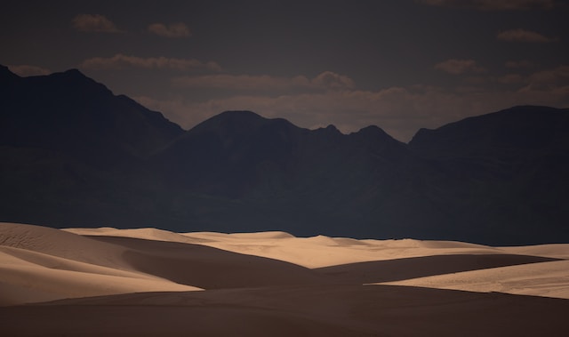 Dark mountains in the background behind sandy hills in the shadows