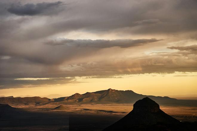 Mountains in a desert at sunset with a cloudy sky abve